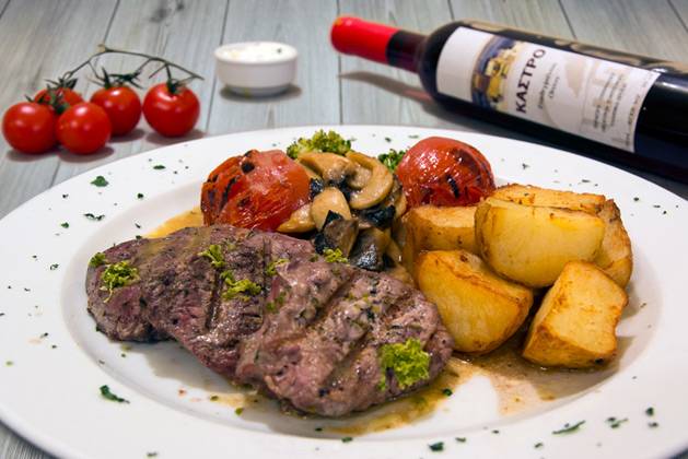 Kastro Oia Restaurant Santorini. Beef fillets on the grill with fresh mushrooms marinated in lime and garnished with baked potatoes and grilled tomatoes.